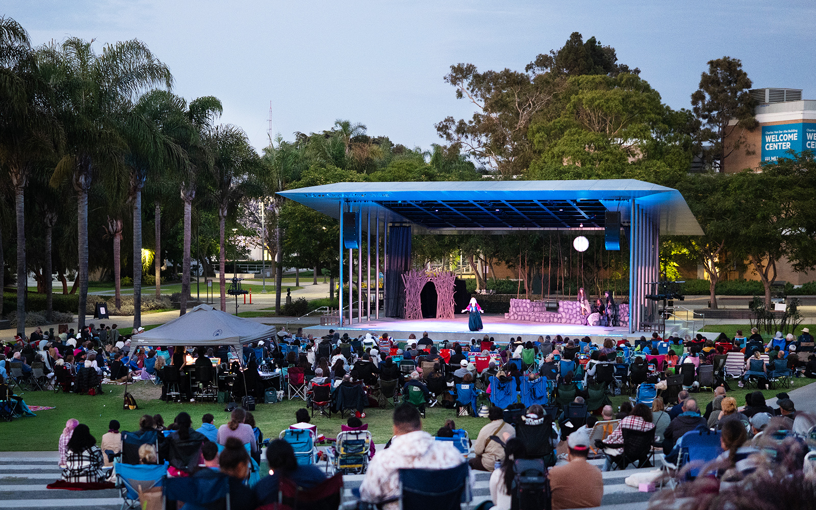 An outdoor theatre performance on a stage with a large audience at night