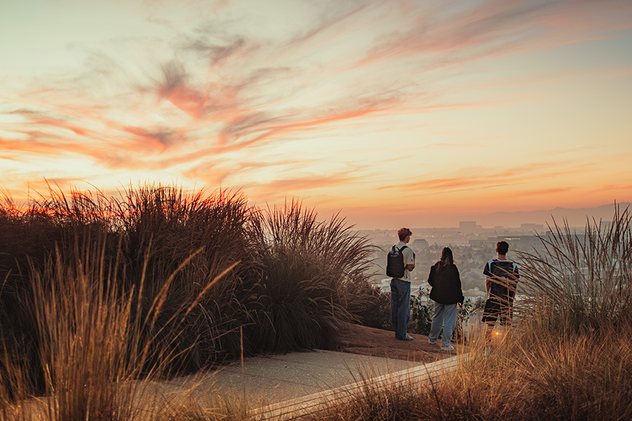 Three students standing at the bluff looking out across Los Angeles at sunset